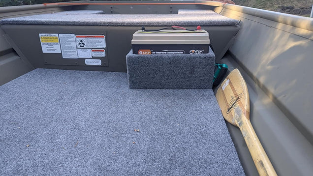 Power Queen 12V Lithium LiFePO4 Battery in a boat with a wooden oar on a gray floor