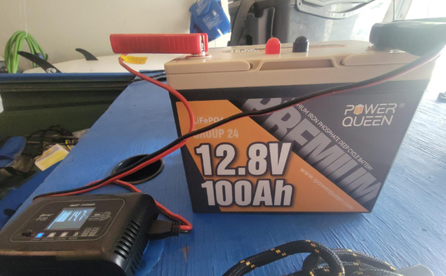 Power Queen 12v 100ah deep cycle battery with charging equipment on a blue surface