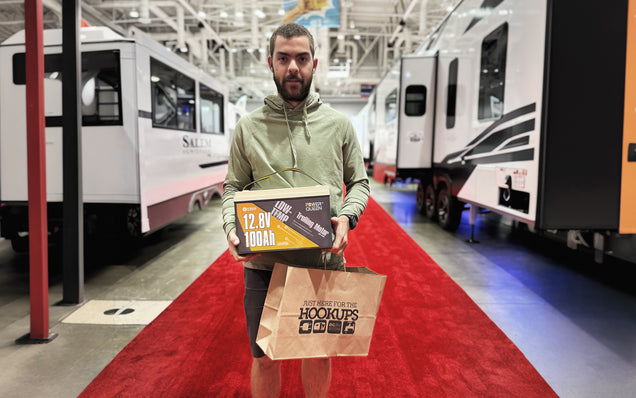Man holding Power Queen 12v 100ah deep cycle battery with RVs in the background