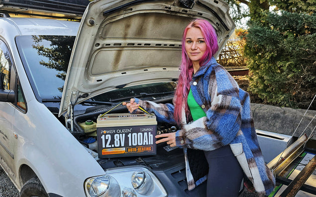 Person with pink hair holding a power queen lithium battery next to an open car hood.