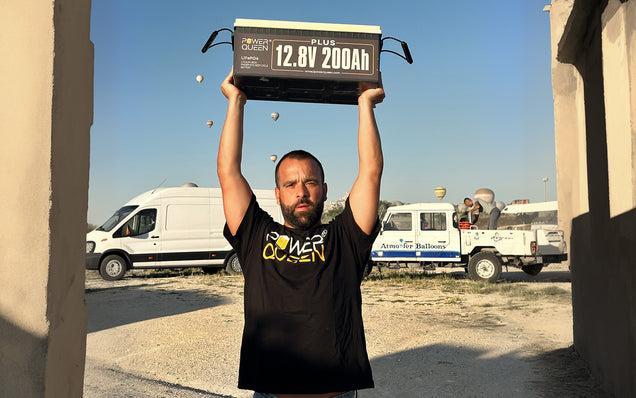 Person lifting a power queen 12v 200ah plus lifepo4 battery in an outdoor setting