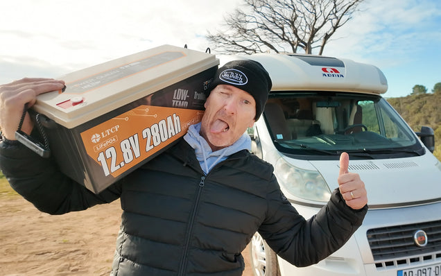 Person holding a large 12v 280ah lifepo4 battery pack with a camper van in the background