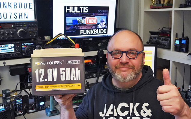 Person holding a Power Queen lithium battery in a room with electronic equipment