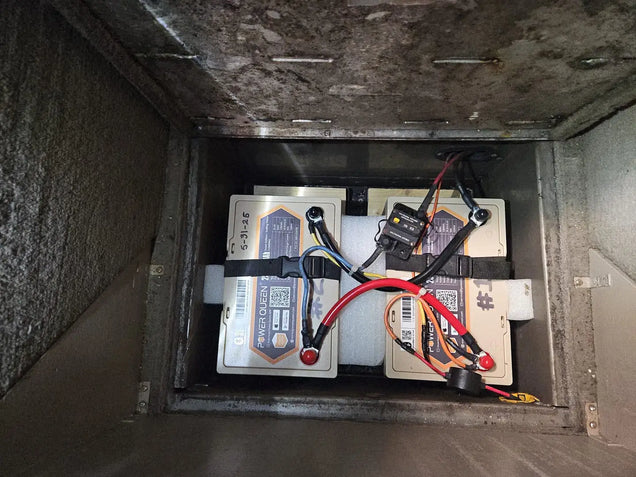 Power Queen 24V LiFePO4 batteries compartment with batteries and connections inside a vehicle.