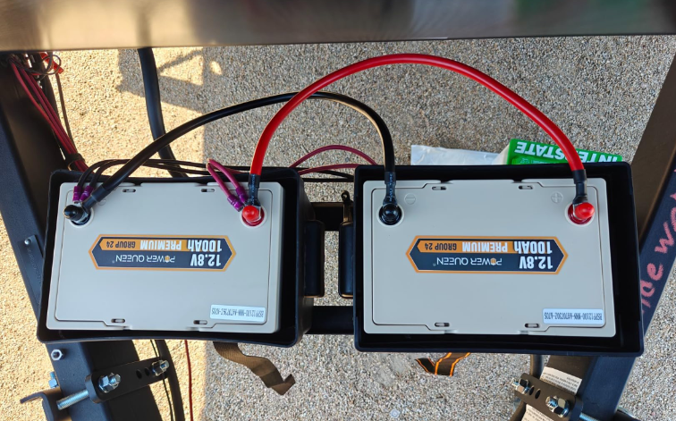 Two 12v 100ah deep cycle battery packs with visible labels on a concrete surface.