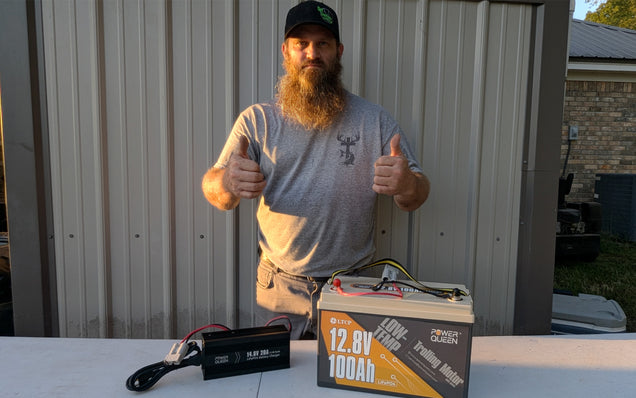 Man giving a thumbs-up with a deep cycle lithium battery and charger on a table outdoors.