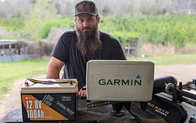 Man with beard and cap sitting outdoors with power queen lithium battery pack.