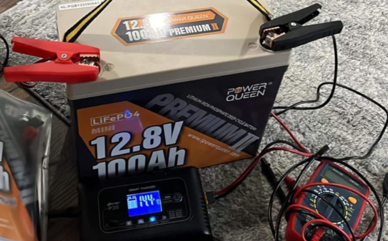 Power Queen lithium battery pack with clamps and digital display on a concrete surface