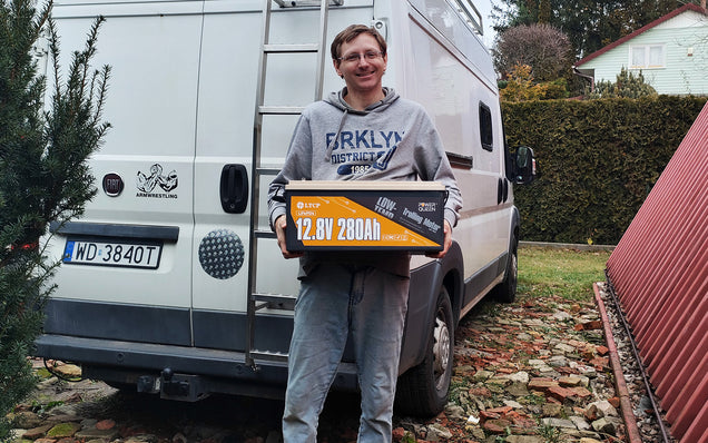 Person holding a Power Queen lithium battery pack in front of a van