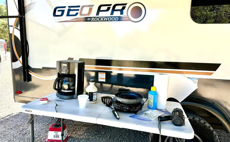 Portable table with coffee maker and bottles in front of Rockwood RV powered by Power Queen lithium battery