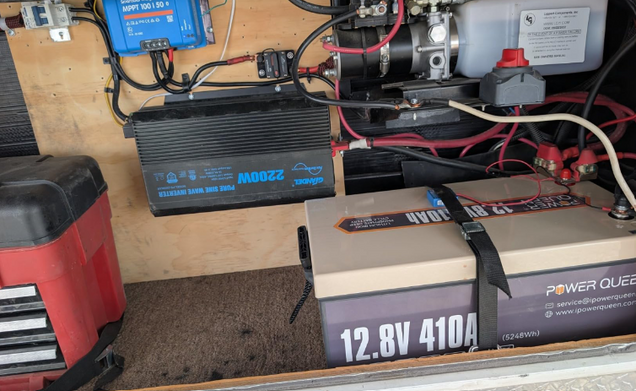 Electrical components including deep cycle lithium batteries and wiring on a wooden surface.