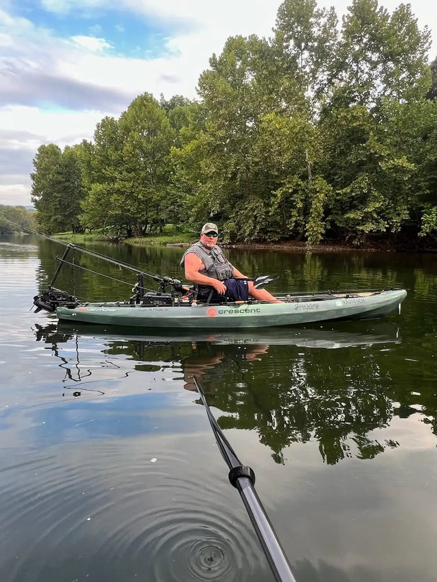 Person fishing from a kayak on a calm lake with trees in the background