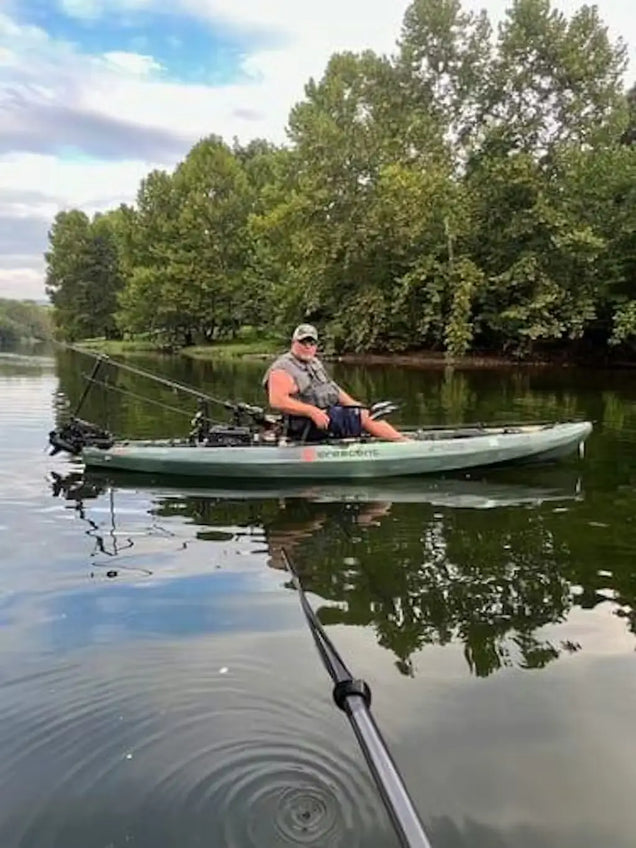 Person fishing from a kayak on a calm lake with trees in the background